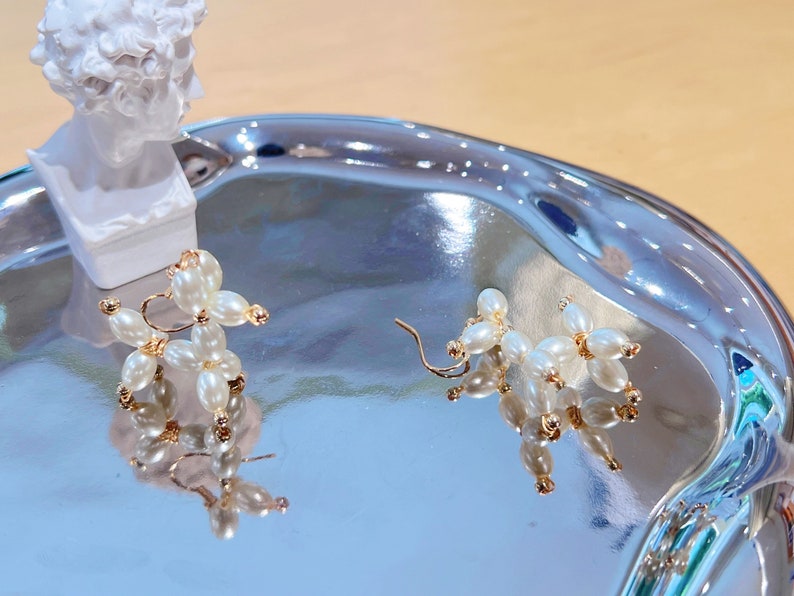 May include: A pair of gold earrings shaped like balloon dogs, made with white pearl beads.