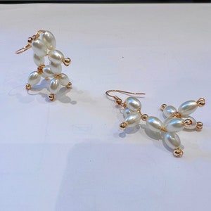 May include: A pair of gold earrings with white pearl beads. The earrings are shaped like a dog