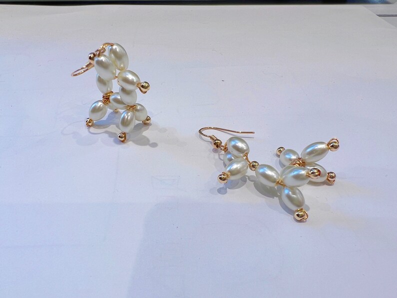 May include: A pair of gold earrings with white pearl beads. The earrings are shaped like a dog