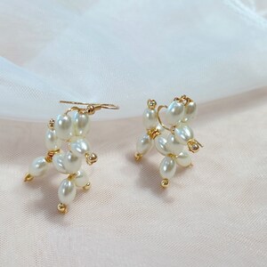 May include: A pair of gold earrings with white pearl accents. The pearls are arranged in a cluster to form a unique design.