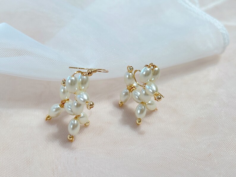 May include: A pair of gold earrings with white pearl accents. The pearls are arranged in a cluster to form a unique design.
