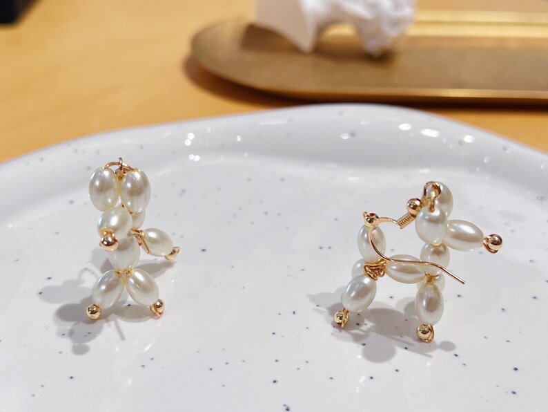 May include: A pair of pearl and gold earrings shaped like a poodle. The earrings are on a white surface.