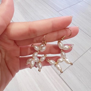 May include: A pair of gold earrings with white pearl beads arranged in a flower shape.