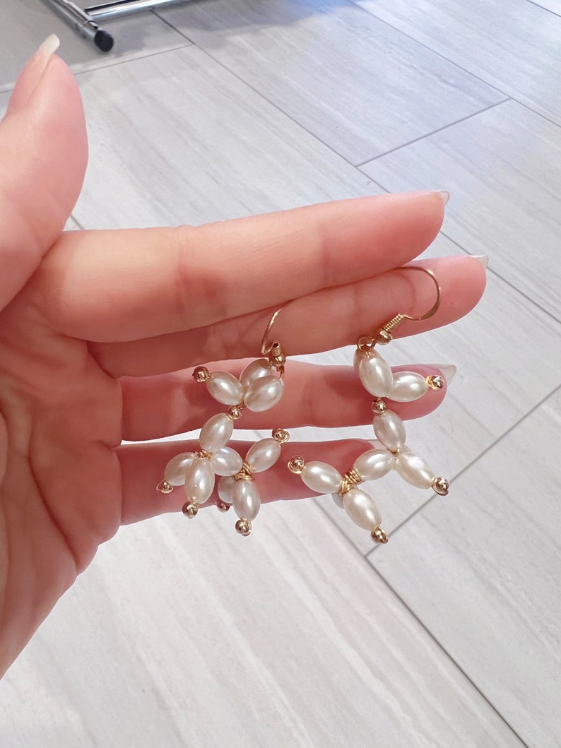 May include: A pair of gold earrings with white pearl beads arranged in a flower shape.