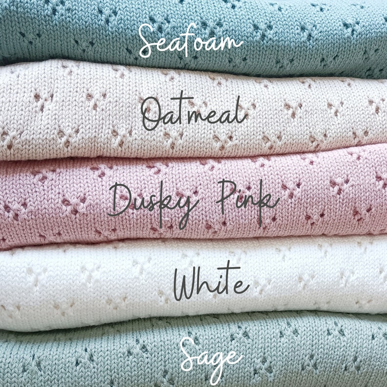 May include: A stack of five knitted blankets in various colors: Seafoam, Oatmeal, Dusky Pink, White, and Sage. Each blanket features a delicate openwork pattern. The names of the colors are written in cursive on the blankets.