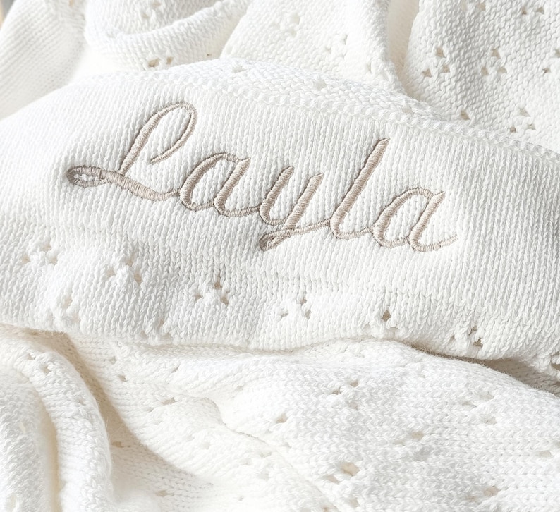 May include: White crocheted baby blanket with the name "Layla" embroidered in a light brown thread.