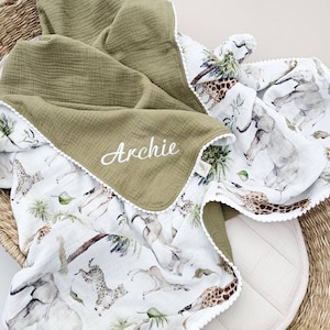 May include: A green and white baby blanket with a white lace trim. The blanket features a watercolor print of animals, including giraffes, elephants, and zebras. The blanket is personalized with the name "Archie" in white embroidery.