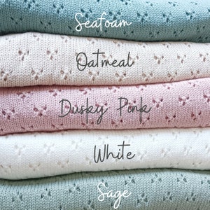 May include: Five knitted blankets stacked on top of each other. The blankets are in the colors sage, white, dusky pink, oatmeal, and seafoam. The colors are written on each blanket.