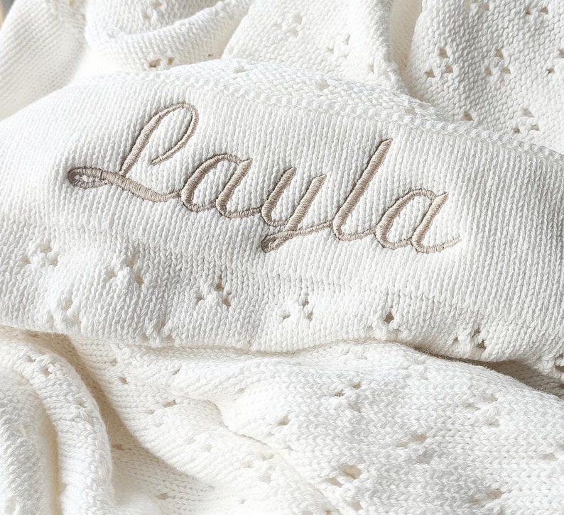 May include: White crocheted baby blanket with the name "Layla" embroidered in beige thread.