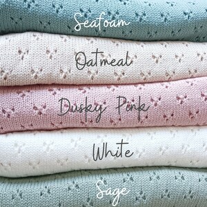 May include: A stack of five knitted blankets in different colors: sage, white, dusky pink, oatmeal, and seafoam. The blankets are folded and stacked on top of each other.