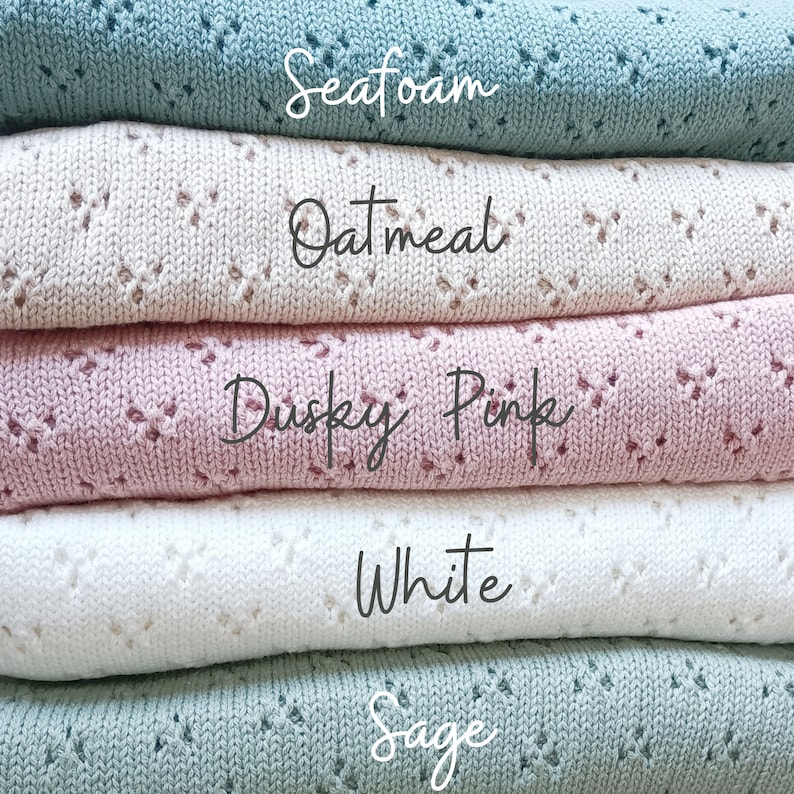 May include: A stack of five knitted blankets in different colors: sage, white, dusky pink, oatmeal, and seafoam. The blankets are folded and stacked on top of each other.