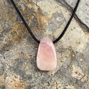 Peut inclure: Un pendentif en quartz rose rose sur un collier en cordon noir. Le pendentif est en forme de larme et a une finition naturelle et polie.