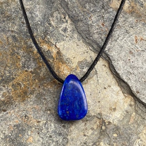 Peut inclure: Un pendentif en lapis-lazuli bleu foncé sur un collier en cordon noir. Le pendentif est en forme de larme et a une texture naturelle et rugueuse.