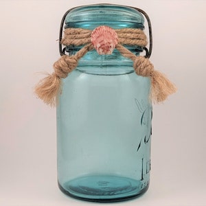 May include: A blue glass jar with a metal lid and a rope tied around the top. A small seashell is tied to the rope.