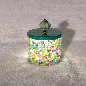 May include: A green glass jar with a green knob lid. The jar is filled with colorful confetti.