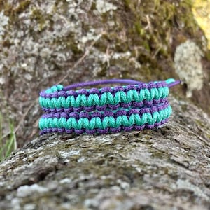 May include: A woven bracelet with alternating bands of teal and purple.