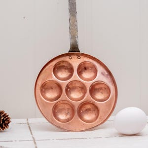 Puede incluir: Una taza de cerámica blanca con un asa negra y el texto "But First, Coffee" en negro y negrita. La taza está sobre una superficie blanca. La taza mide aproximadamente 10 cm de alto.