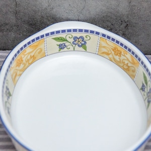 May include: White ceramic serving dish with a floral design. The rim features a blue and yellow floral pattern with blue accents. The dish has a rounded shape with a slightly raised edge and two small handles.