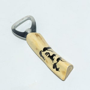 Puede incluir: Un abridor de botellas con un mango de madera que presenta un diseño en blanco y negro de una cabeza de lobo. La parte metálica del abridor es plateada.