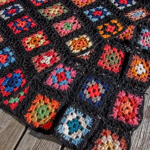 May include: A black crochet blanket with colorful granny squares. The blanket is made of yarn in various colors, including red, blue, green, yellow, and orange.