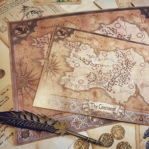 Op de afbeelding: Een vintage-stijl kaart van een fictief continent met de titel "The Continent" en de woorden "Emerald Sea" en "Arcelia Ocean" erop gedrukt. De kaart is omgeven door decoratieve randen en ligt op een tafel met andere papieren en een pen.