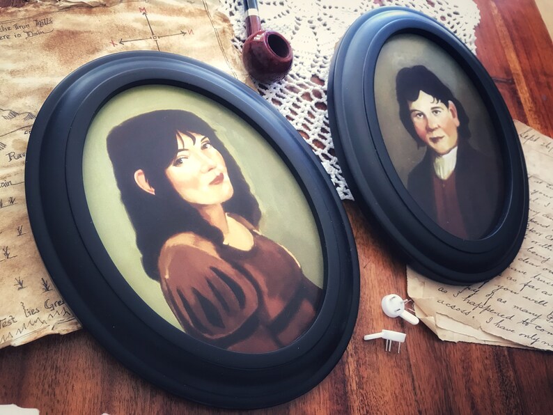 May include: Two oval-framed portraits with black frames. One portrait features a woman with dark hair and a brown dress. The other portrait shows a man in a dark coat and white shirt. A pipe and paper are in the background.