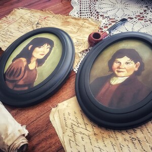 May include: Two oval framed portraits with black frames. The portraits depict individuals with dark hair and are set against a green background. A pipe, aged paper, and a rolled scroll are also visible, suggesting a vintage theme.