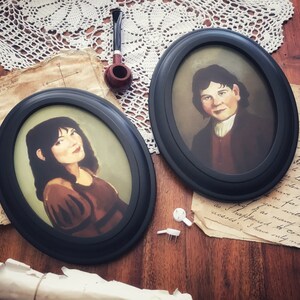 May include: Two oval black framed portraits of people with dark hair. One portrait shows a person in a brown top, the other a person in a dark jacket. A pipe and aged paper with text are also visible.