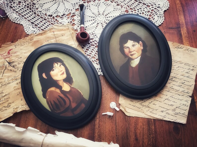 May include: Two oval black framed portraits of people with dark hair. One portrait shows a person in a brown top, the other a person in a dark jacket. A pipe and aged paper with text are also visible.