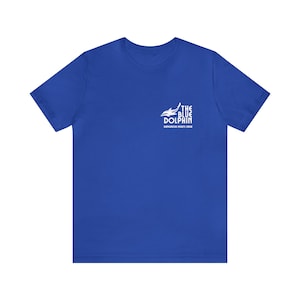 Può includere: T-shirt blu reale con una grafica bianca di un delfino e il testo "The Blue Dolphin" e "Dolphins Rights Club".