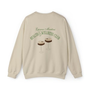 May include: A beige sweatshirt with the text "Espresso Martini Health & Wellness Club" in green lettering and a graphic of two espresso martinis.