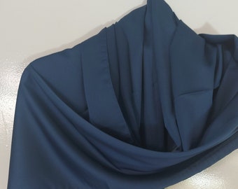 May include: A teal-coloured scarf made from a smooth, flowing fabric. The scarf is draped and hangs against a white background, highlighting its elegant drape and rich colour. The fabric appears to be lightweight and soft.