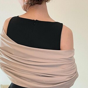 May include: A black sleeveless dress with a beige shawl draped over the shoulders. The shawl is folded and gathered, creating a soft and elegant look.