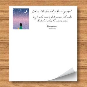 May include: A white print with a quote by Stephen Hawking, "Look up at the stars and not down at your feet." The print features a person looking at a starry sky with a crescent moon. The quote ends with "Be curious."