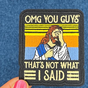 May include: A black and yellow embroidered patch with a retro-style image of Jesus with his hand over his face. The text on the patch reads "OMG YOU GUYS THAT'S NOT WHAT I SAID".
