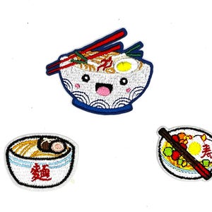 May include: Embroidered patches featuring ramen bowls with various designs. One patch shows a smiling bowl with chopsticks, another has Japanese text, and the third has an egg and chopsticks. The patches are colorful.