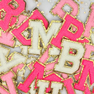May include: A pile of pink, white, and gold felt letters with a glittery finish. The letters are in various sizes and are arranged in a random order.