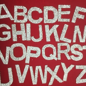 May include: A full alphabet set of iron-on rhinestone letters in silver. Each letter is made of small, clear rhinestones.