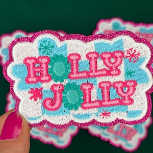 May include: A pink and blue embroidered patch with the words "Holly Jolly" in a white and blue checkered pattern.