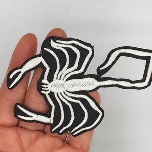 May include: White embroidered scorpion patch on a black background. The scorpion is facing right and has a curled tail.