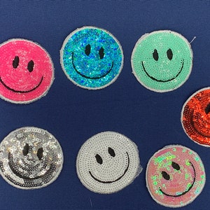 May include: Seven colorful smiley face patches with sequins. The patches are in various colors including pink, blue, green, silver, white, and red.