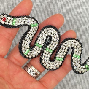 May include: A black and green snake-shaped beaded applique with rhinestones and green accents.