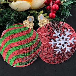 May include: Two Christmas ornament patches, one red with a white snowflake and one red and green striped. Both are made of sequins.