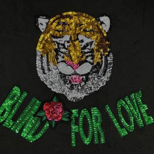 May include: A black fabric patch with a green sequined design that says "Blind for Love". A gold and white sequined tiger face is above the text.