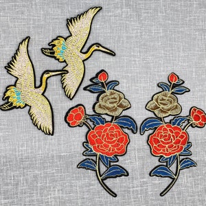 May include: Two embroidered yellow cranes with gold accents and two embroidered red and gold flowers with blue leaves.