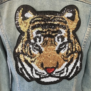 May include: A denim jacket with a large sequined tiger head patch. The tiger is gold, black, and white with a red nose.