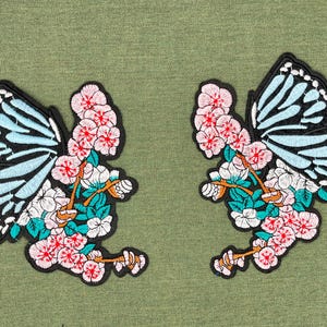 May include: Two embroidered iron-on patches featuring a blue butterfly with black wings and pink and white flowers.