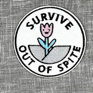 May include: White embroidered patch with black text that reads "Survive Out of Spite" and a pink and blue flower with a smiling face.