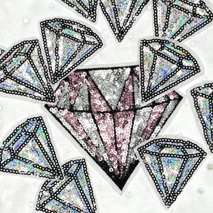 May include: A collection of sequined diamond patches in various sizes. The diamonds feature iridescent sequins with black borders. One large diamond patch has pink and silver sequins. The patches are scattered on a white surface.