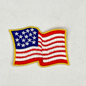 May include: A red, white, and blue embroidered American flag patch with a yellow border. The flag is waving in the wind.